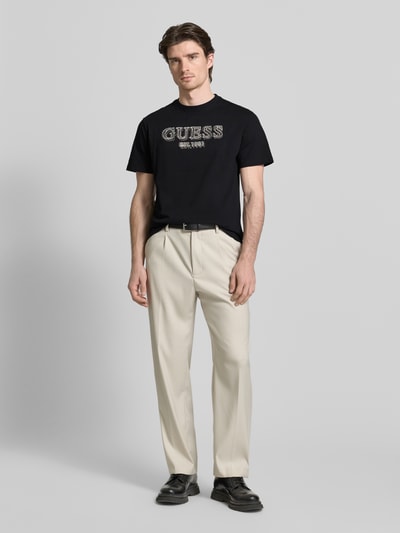 Męski model trägt T-shirt mit Label-Detail von GUESS, czarny, bawełna, krój regular fit, okrągły dekolt, długość tyłu 69 cm, Ganzkörperansicht von vorne