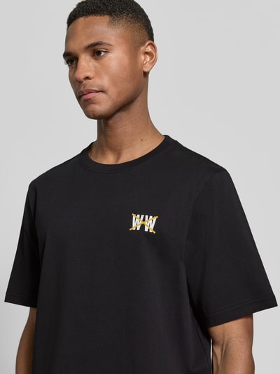 Männermodel trägt Regular Fit T-Shirt mit Logo-Print Modell 'Bobby' von Wood Wood in Schwarz aus reiner Baumwolle, Nahaufnahme Oberkörper.