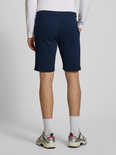 Männermodel trägt dunkelblaue Shorts mit Logo-Print Modell 'GORDON' von Jack & Jones aus Baumwoll-Mix, Ganzkörperansicht Rückansicht.