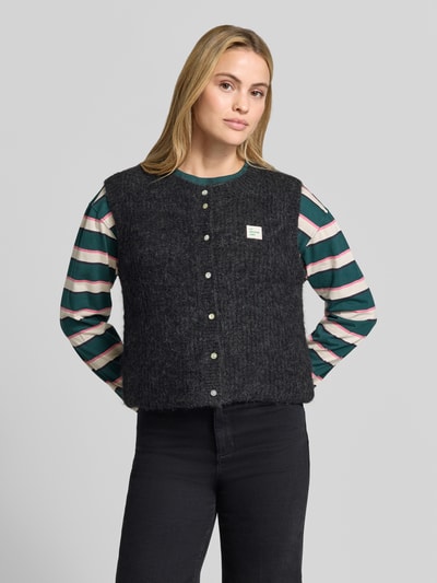 Frauenmodel trägt Regular Fit Weste mit Alpaka-Leinen-Anteil Modell 'EAST' von American Vintage, Strick-Optik, Logo-Detail, Nahaufnahme Oberkörper.