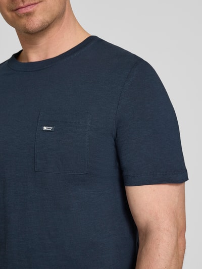 Męski model nosi Regular Fit T-Shirt aus reiner Baumwolle von s.Oliver RED LABEL w kolorze jednolitej melanżowej granatowej, z krótkim rękawem, okrągłym dekoltem, kieszenią na piersi, naszywką z logo, materiał bawełna, zbliżenie na górną część ciała.