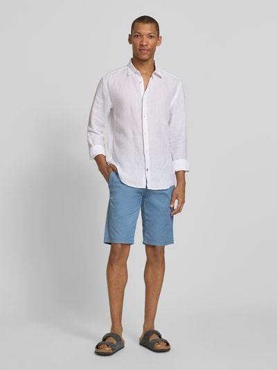 Männermodel trägt Slim Fit Chinoshorts aus Baumwoll-Mix von Tom Tailor, efekt: wzór na całej powierzchni, krój slim fit, tkany wzór, aplikacja z logo, szlufki na pasek, zapięcie na guzik i ukryty zamek błyskawiczny, wpuszczane kieszenie, kieszenie z tyłu, wykończenie materiału: splot twill, mieszanka bawełny, jasnoniebieski odcień, gładka tekstura, Ganzkörperansicht von vorne.