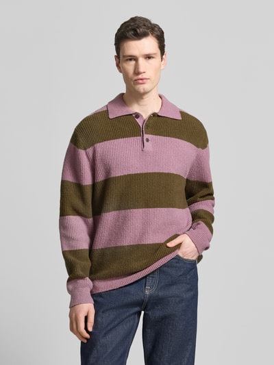 Männermodel trägt Strickpullover mit Polo-Kragen Modell 'Kimse' von Wood Wood, breite rosa und olivgrüne Blockstreifen, Baumwoll-Mix, Ganzkörperansicht von vorne.