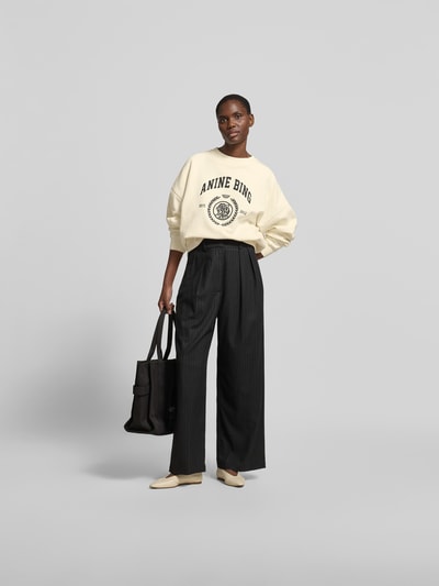 Frauenmodel trägt Oversized Sweatshirt mit Logo-Print von Anine Bing in Creme, Reine Baumwolle, Oversized-Fit, Rundhalsausschnitt, elastische Abschlüsse, Rückenlänge bei Größe S 61 cm, Ganzkörperansicht von vorne.