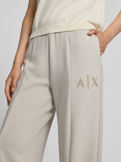 Vrouwenmodel draagt Straight Fit Sweatpants uit elastische viscosemix van Armani Exchange, labeldetail, pijpsplit, elastische band, lichte beige kleur, structuur glad, Binnenbeenlengte bij maat S 77 cm, detailopname bovenbeen.