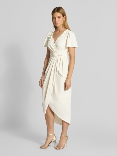 Frauenmodel trägt Cocktailkleid in Wickel-Optik mit Schmetterlingsärmeln von Christian Berg Cocktail in Satin, cremefarben, tailliert, Midilänge, V-Ausschnitt, mit Bindegürtel, verlängerter Rücken, Rückseite mit Haken- und Reißverschluss, Ganzkörperansicht von vorne