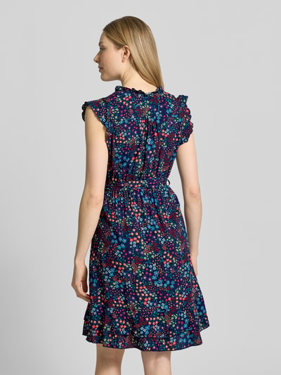 Frauenmodel trägt Minikleid aus reiner Viskose mit floralem Allover-Print von Apricot in Dunkelblau mit buntem Muster, Taille betont, Rüschen an Ärmeln und Rocksaum, Knopfleiste, abnehmbares Taillenband, ärmellos, feine Stoffstruktur, Ganzkörperansicht Rückansicht.