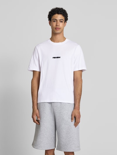 Męski model nosi T-Shirt mit Logo und Rundhalsausschnitt od REVIEW, bawełna, krój relaxed fit, długość tyłu w rozmiarze M: 68 cm, Ganzkörperansicht von vorne.
