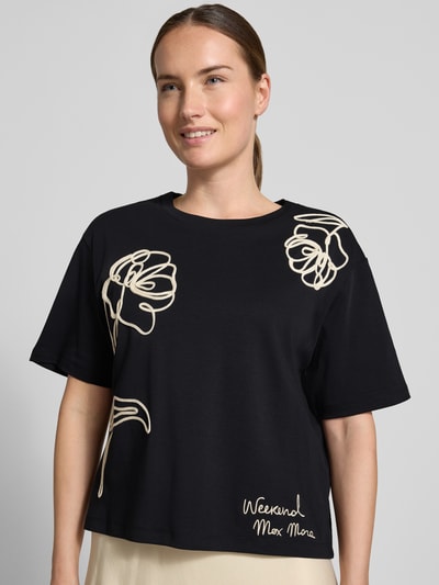 Vrouwenmodel draagt Boxy Fit t-shirt van puur katoen model 'SALA' van Weekend Max Mara, zwart met crèmekleurige prints, Nahaufnahme Oberkörper.