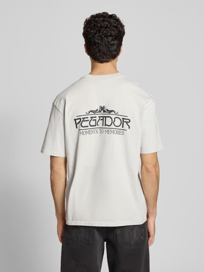 Männermodel trägt Oversized T-Shirt aus Baumwolle Modell 'Stavoren' von Pegador, Weiß, dunkler Print, Rückenlänge 70 cm, Ganzkörperansicht Rückansicht.