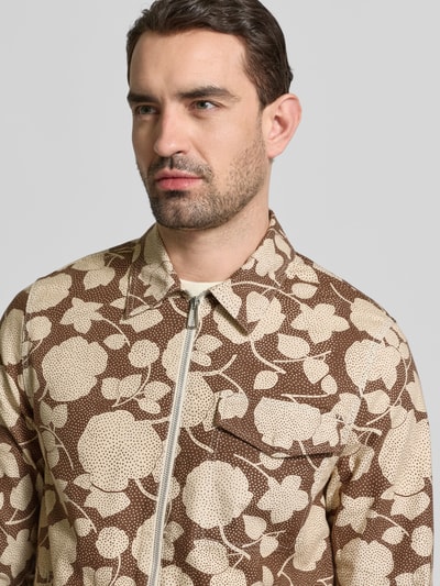 Männermodel trägt Jacke im Allover-Look mit Brusttasche von PAUL SMITH in Braun und Beige, reine Baumwolle, Nahaufnahme Oberkörper. Regular Fit mit Umlegekragen und Reißverschluss, sichtbare Brusttasche, strukturierte Textur.