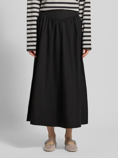 Frauenmodel trägt schwarzen Midirock mit A-Linie aus reiner Baumwolle, seitlicher Reißverschluss, Modell 'SALLY' von Topshop, Bundweite 35 cm, Ganzkörperansicht von vorne.