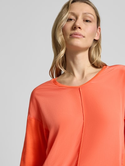 Modelka kobieca ma na sobie damski t-shirt z mieszanki bawełny i elastanu Marc Cain, prosty krój, dekolt w serek, ozdobne szwy, rękaw o dł. 3/4, detal z logo, długość tyłu przy rozmiarze 36: 60 cm, widok z przodu zbliżenie na górną część ciała.