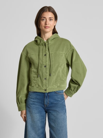 Kobiece model nosi Jeansjacke mit Kapuze und Eingrifftaschen von Marc Cain, mieszanka bawełny z dodatkiem streczu, krój regular fit, kaptur z trokiem, zapięcie na zatrzask, wpuszczane kieszenie, długość tyłu w rozmiarze 36: 51 cm, szerokość ramion w rozmiarze 36: 53 cm, szerokość klatki piersiowej w rozmiarze 36: 52 cm, długość rękawów w rozmiarze 36: 54 cm, zielony, proste faktury, widok całej sylwetki z przodu.