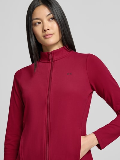 Frauenmodel trägt Slim Fit Trainingsjacke mit Logo-Print von Under Armour in Dunkelrot mit Reißverschluss, glatte Textur, Nahaufnahme Oberkörper, Damen Trainingsjacke von Under Armour.
