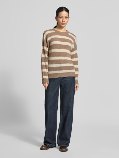 Frauenmodel trägt Strickpullover mit Woll-Anteil Modell 'Festina Hope' von MSCH Copenhagen, beige-braune Streifen, gerader Schnitt, Rundhalsausschnitt, Material-Mix, überschnittene Schultern, kombiniert mit dunkelblauen Jeans, Ganzkörperansicht von vorne.