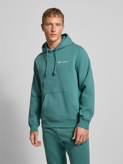 Männermodel trägt Hoodie mit Kapuze von CHAMPION aus Baumwoll-Mix in Türkis, Lockerer-Schnitt, Label-Stitching, Känguru-Tasche, Gerippte-Abschlüsse, Ganzkörperansicht von vorne.