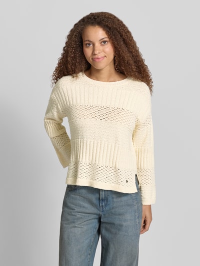 Frauenmodel trägt Boxy Fit Strickpullover aus reiner Baumwolle Modell 'ALAYA' von Pepe Jeans, Strickoptik, Struktur, Rundhals, Langarm, asymmetrisch, Materialverarbeitung Strick, Farbe Creme, ganzkörperansicht von vorne.