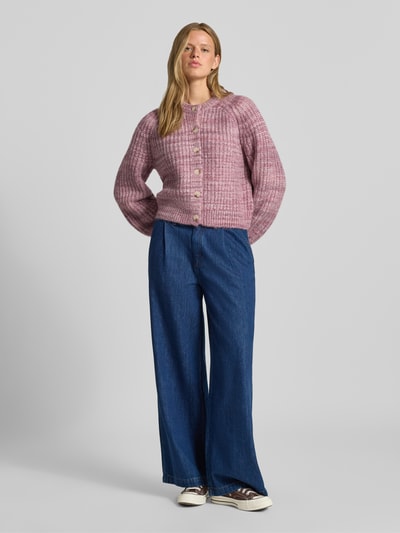 Frauenmodel trägt Cardigan mit Woll-Anteil und Rundhalsausschnitt von REVIEW, gerade geschnitten, Knopfleiste, rosa Textur, Ganzkörperansicht von vorne.