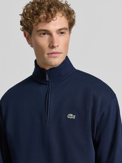 Männermodel trägt Regular Fit Troyer aus Baumwoll-Mix von Lacoste in Dunkelblau mit glatter Textur, Nahaufnahme Oberkörper, Herren Troyer von Lacoste.