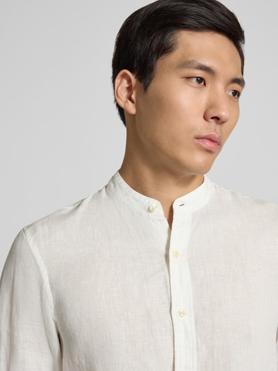 Männermodel trägt Regular Fit Leinenhemd mit Stehkragen von Scotch & Soda in Offwhite, feine Textur, reine Leinenqualität, Nahaufnahme Oberkörper.