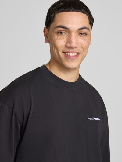 Męski model nosi Oversized T-Shirt mit Logo-Stitching von Pegador z bawełny, krój oversized fit, okrągły dekolt, wyhaftowane logo, zbliżenie na górę ciała.