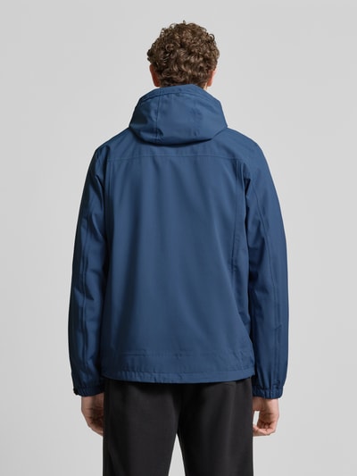 Männermodel trägt blaue Jacke mit Napoleontasche Modell 'KOS' von Killtec, gerade Passform, Kapuze, Ganzkörperansicht Rückansicht.
