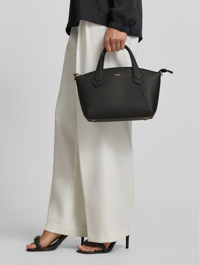 Kobiece modelka trzyma Henkeltasche aus echtem Leder Modell 'LENAH' od BOSS, czarne gładkie licowe skóry, złote detale, przód, zbliżenie na torebkę.