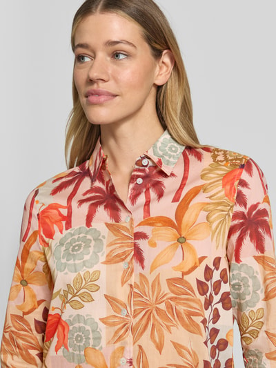 Frauenmodel trägt Regular Fit Bluse im Allover-Look von Christian Berg Woman aus reiner Baumwolle, florale Muster in Orange, Grün und Beige, Hemdblusenkragen, Nahaufnahme Oberkörper.