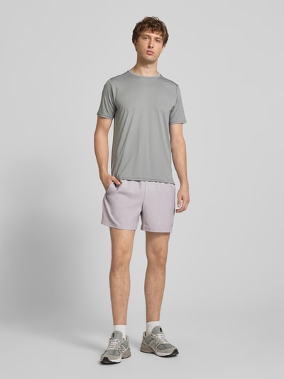 Männermodel trägt Shorts mit elastischem Bund und Logo von New Balance in Hellgrau, Regular Fit, Logo am Bein, Ganzkörperansicht von vorne.
