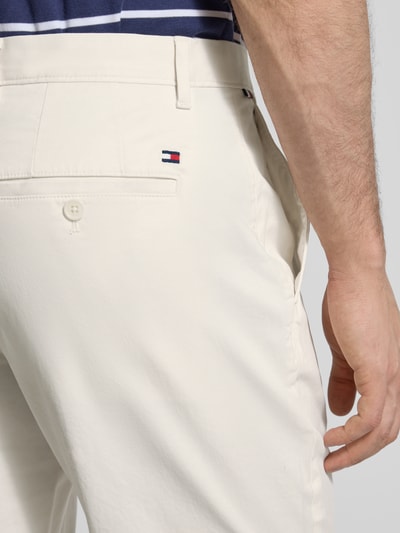 Mężczyznamodel nosi Slim Fit Chino aus Baumwoll-Mix von Tommy Hilfiger, kolor jednolity, bawełniany materiał, tylne kieszenie z guzikiem, detal z logo, krój slim fit, ujęcie z tyłu zbliżenie na biodra.