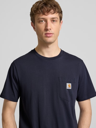 Męski model nosi Regular Fit T-Shirt mit Logo-Patch od Carhartt Work In Progress, czysta bawełna, krój regular fit, naszywka z logo, kieszonka na piersi, dekolt okrągły, długość pleców w rozmiarze M: 70 cm, ciemny granat, prosty fason, gładka faktura, zbliżenie na górną część ciała z przodu.
