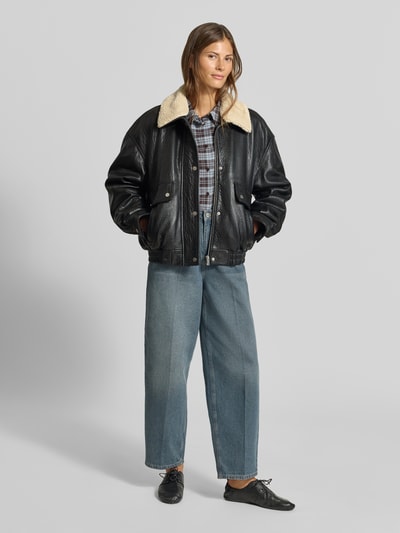 Frauenmodel trägt Regular Fit Bomberjacke mit Umlegekragen von MYON, schwarze Lederoptik, beige Kragen, Eingrifftaschen, elastischer Bund, Ganzkörperansicht von vorne.