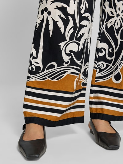 Frauenmodel trägt Wide Fit Stoffhose mit floralem Allover-Print von Emily Van den Bergh in Schwarz, Weiß und Braun aus reiner Baumwolle, elastischer Bund, Detailaufnahme Beine.