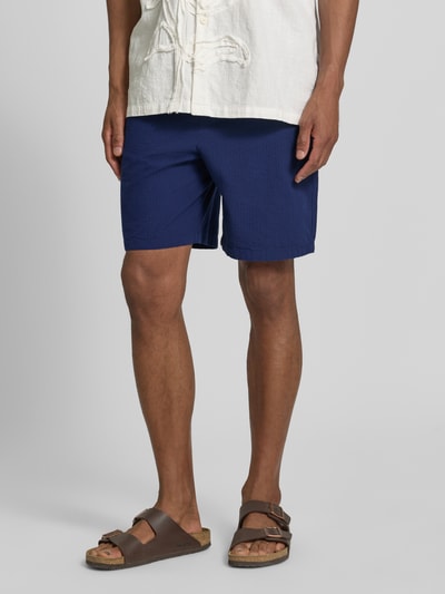 Männermodel trägt Regular Fit Shorts aus reiner Baumwolle Modell 'STUART' von SELECTED HOMME in Uniblau, Seersucker-Textur, Nahaufnahme Oberschenkel.