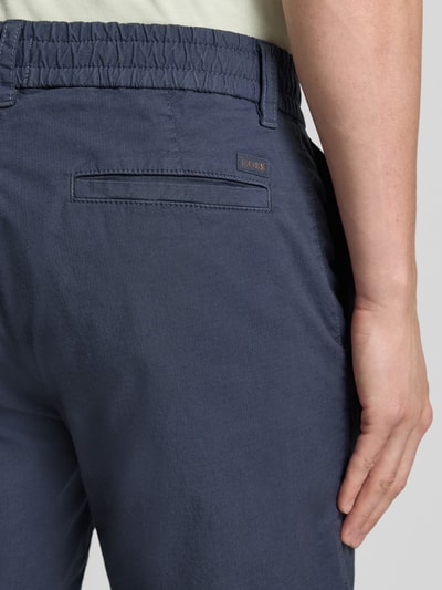 Männermodel trägt dunkelblaue Tapered Chinoshorts aus Baumwoll-Mix Modell 'CHINO_TAPERED_DS_3S' von BOSS Orange, Detailaufnahme Rückansicht.