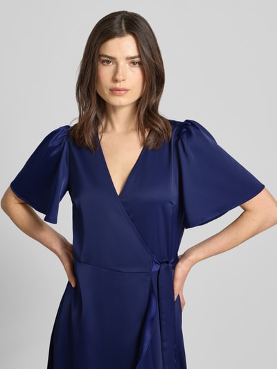 Vrouwenmodel draagt Cocktailkleid mit Volantsaum Modell 'THEA' van YAS, satijn, getailleerde fit, wikkel-look, V-hals, vlindermouwen, midijurk, kleur blauw, detailopname bovenlichaam.