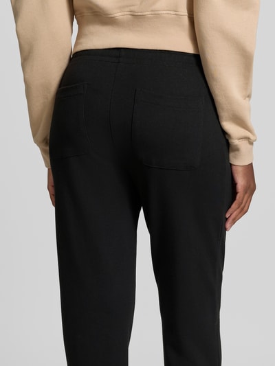 Frauenmodel trägt Sweatpants in verkürzter Passform von Juvia in Schwarz, aus Baumwoll-Modal-Mix mit geradem Schnitt und Eingrifftaschen, Nahaufnahme Rückansicht.