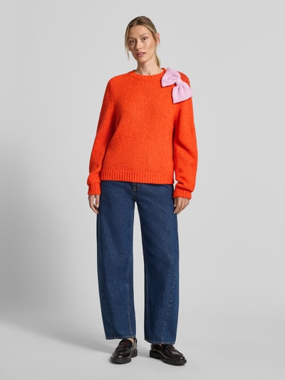 Frauenmodel trägt Relaxed Fit Pullover aus Baumwoll-Mix Modell 'KOLLIER' von Essentiel Antwerp in Orange mit rosa Schleifendetail, Ganzkörperansicht von vorne. Damen Pullover von Essentiel Antwerp.