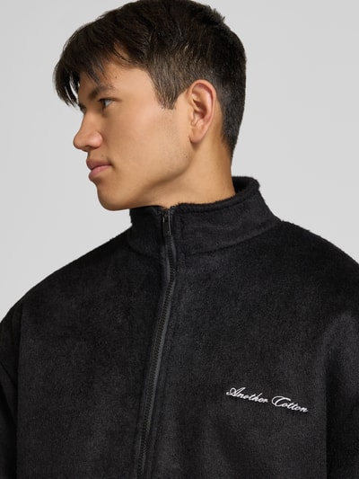 Männermodel trägt Fleecejacke mit Label-Stitching und Zweiwege-Reißverschluss von ANOTHER COTTON LAB, Schwarz, Nahaufnahme Oberkörper.