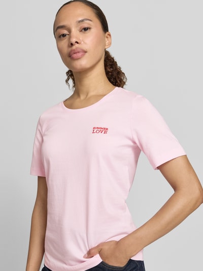 Modelka kobieca ma na sobie damski t-shirt z bawełny, krój regular fit, okrągły dekolt, wyhaftowany napis, Christian Berg Woman, długość tyłu w rozmiarze S: 59 cm, jasnoróżowy z czerwonym napisem, widok na górną część ciała z przodu
