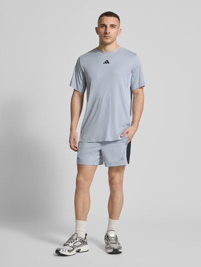 Männermodel trägt Regular Fit Sport-Shorts aus schnelltrocknendem Material von adidas Training, Mehrfarbig, Schriftzug, Logo-Print, perforierte Einsätze, Tunnelzug innen, elastischer Bundabschluss, Funktion: schnelltrocknend, feuchtigkeitsregulierend, seitliche Eingrifftaschen, Ganzkörperansicht von vorne.