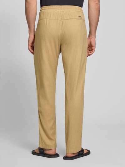 Męski model nosi Wide Fit Leinenhose mit Viskose-Anteil Modell 'Malvin' od Blend, kolor beżowy, elastyczny pas, tylna kieszeń, struktura lnu, Szerokość w rozmiarze M: 38 cm, długość nogawki od wewnątrz: 76 cm, Ganzkörperansicht Rückansicht.