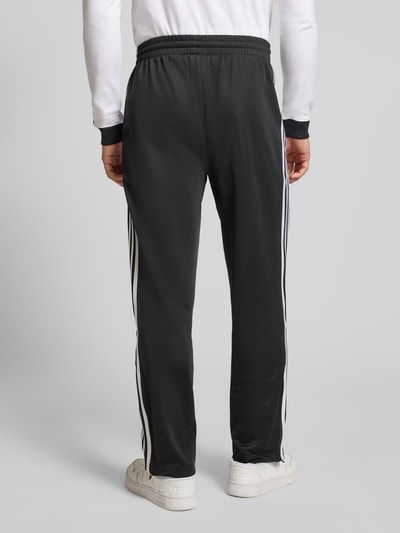 Männermodel trägt Sweatpants mit elastischem Bund von adidas Originals in Schwarz mit weißen Streifen, lockerer Schnitt, Ganzkörperansicht Rückansicht.