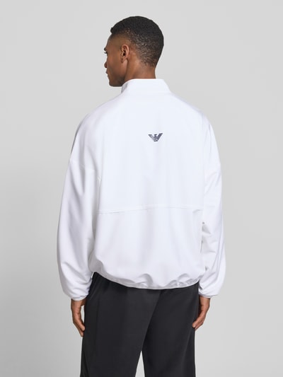 Männermodel trägt weiße Bomberjacke mit Stehkragen und Logo-Print von EA7 Emporio Armani, elastische Abschlüsse, Rückansicht Ganzkörperansicht.