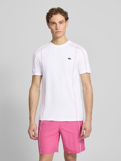 Männermodel trägt Regular Fit T-Shirt mit UV-Schutz 50+ von Lacoste Sport in Weiß mit Kontraststreifen, Logo-Patch, unifarben, Ganzkörperansicht von vorne