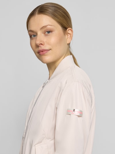 Frauenmodel trägt Regular Fit Bomberjacke mit Stehkragen Modell 'Brooklyn' von Frieda & Freddies in hellem Ton, glatte Struktur, Eingrifftaschen, Reißverschluss, elastische Abschlüsse, Schulterbreite 44 cm, Brustweite 52 cm, Ärmellänge 51 cm, Rückenlänge 59 cm bei Größe 36, Nahaufnahme Oberkörper.