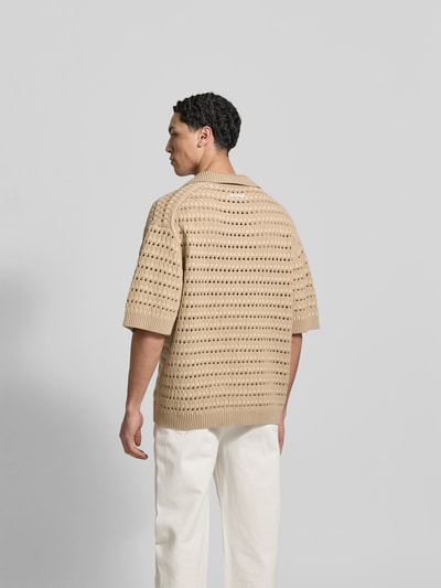Männermodel trägt Relaxed Fit Poloshirt mit Viskose-Anteil von MAISON KITSUNÉ in Beige, Baumwoll-Viskose-Mix, Lochmuster, Halbarm, Ganzkörperansicht Rückansicht.