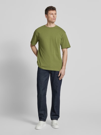 Męski model nosi Relaxed Fit T-Shirt aus Bio-Baumwoll-Mix Modell 'MAARKOS' von Armedangels, zielony, jednokolorowy jersey, wyhaftowane logo, okrągły dekolt, krótki rękaw, mieszanka bawełny ekologicznej, Ganzkörperansicht von vorne.