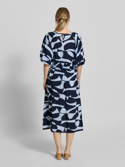 Frauenmodel trägt Midikleid aus Viskose Modell 'CHANISE' von Soyaconcept, A-Linie, Allover-Look, Dunkelblau und Weiß, Rückenlänge 119 cm, Brustweite 48 cm, Ärmellänge 28 cm, Ganzkörperansicht Rückansicht.